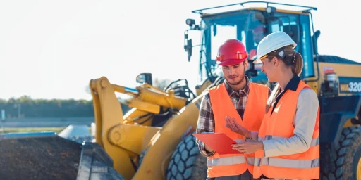 Mann und Frau auf einer Baustelle mit Radlader im Hintergrund, Copyright: Kzenon - stock.adobe.com