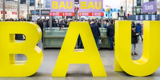 Schriftzug BAU vor dem Hintergrund einer vollen Messehalle, Copyright: Messe München
